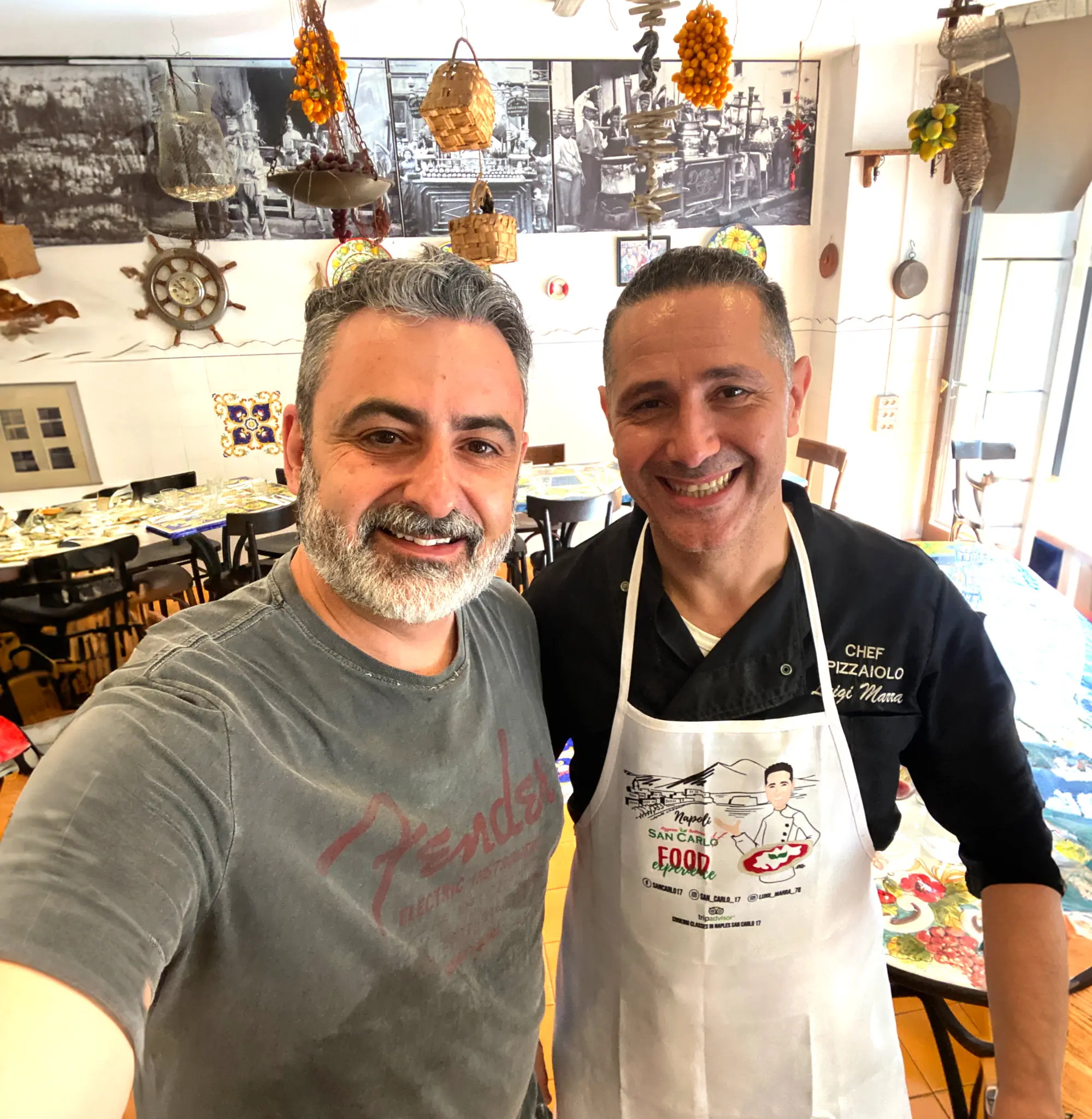 Leo Nelli e o Maestro Luigi Marra posam em um salão com mesas e decoração italiana.