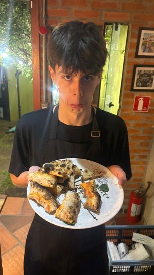 Jovem segura um prato com porções de pizza no interior da Pizzanelli.