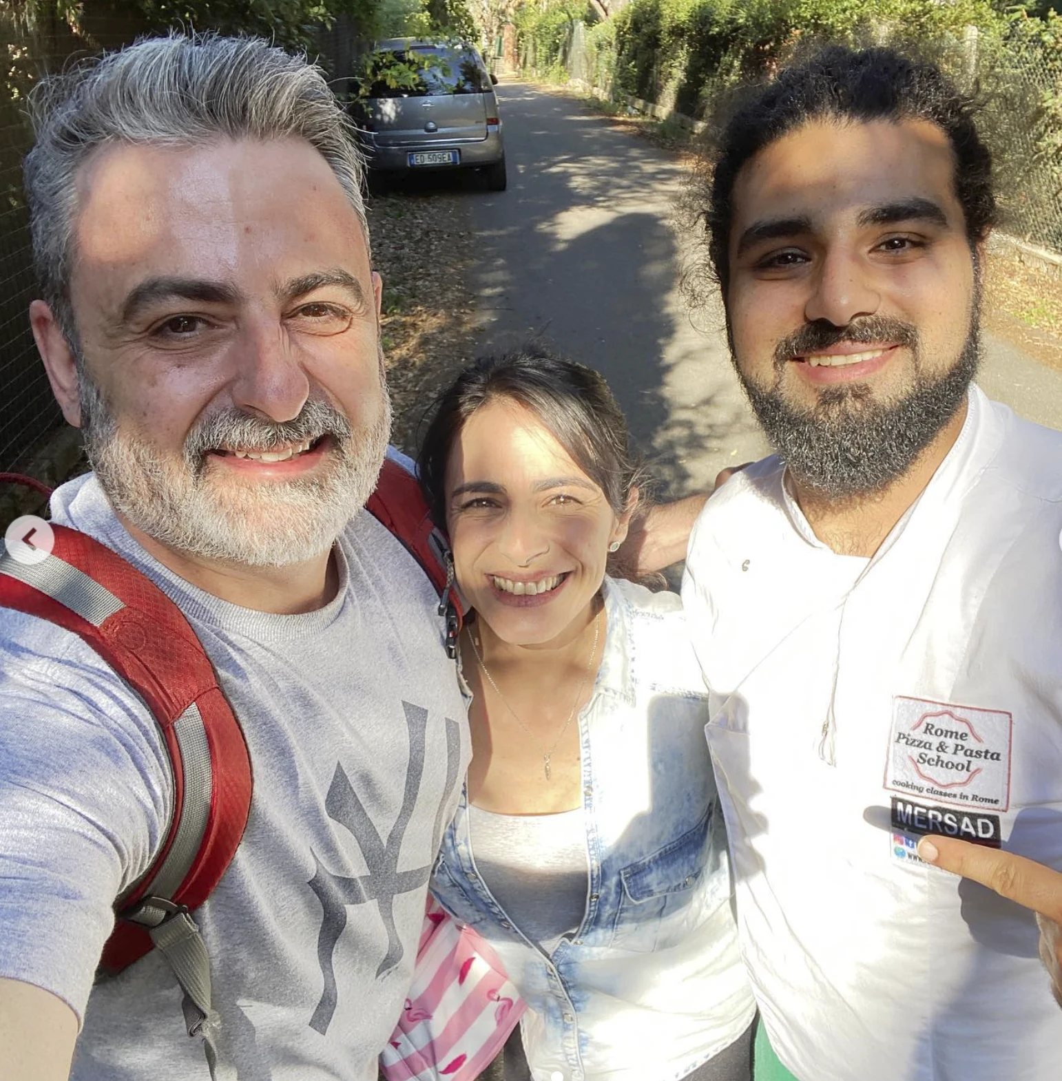 Três pessoas posam ao ar livre; o Maestro Mersad Hatampouri usa a camiseta da Rome Pizza & Pasta School.